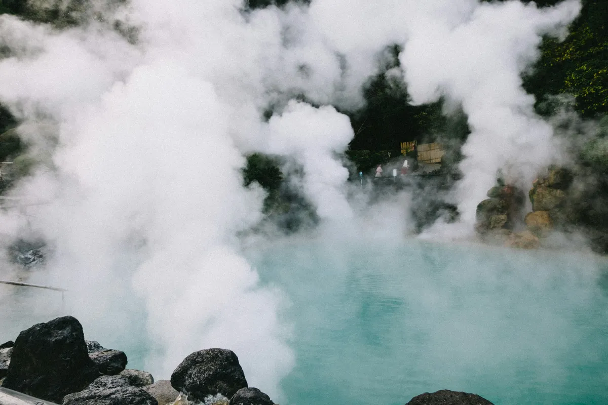 Steaming turquoise hot spring pool surrounded by rocks at a Japanese onsen
