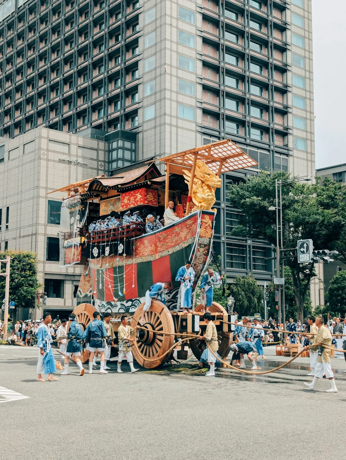 A decorated yamaboko float being pulled through a Kyoto street during the Gion Matsuri parade, with participants in traditional blue happi coats