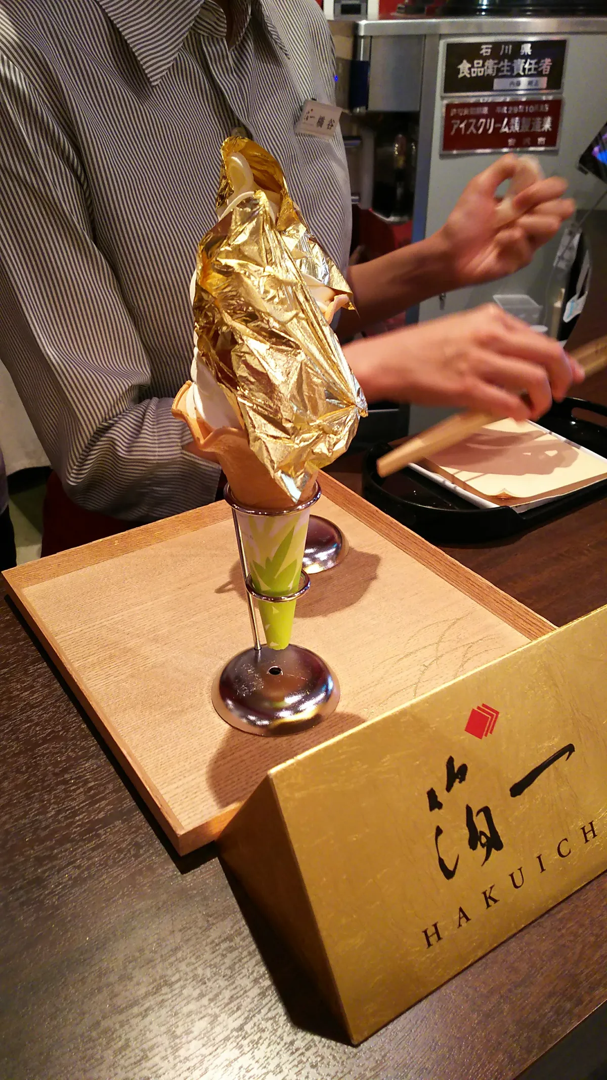 Gold leaf ice cream served on a wooden stand with the Hakuichi logo at a shop in Kanazawa