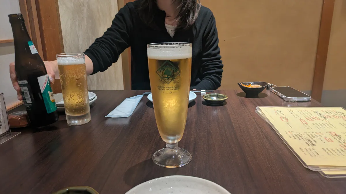 Draft beer glass on a dark wooden table at a Kanazawa izakaya with a handwritten menu in the background
