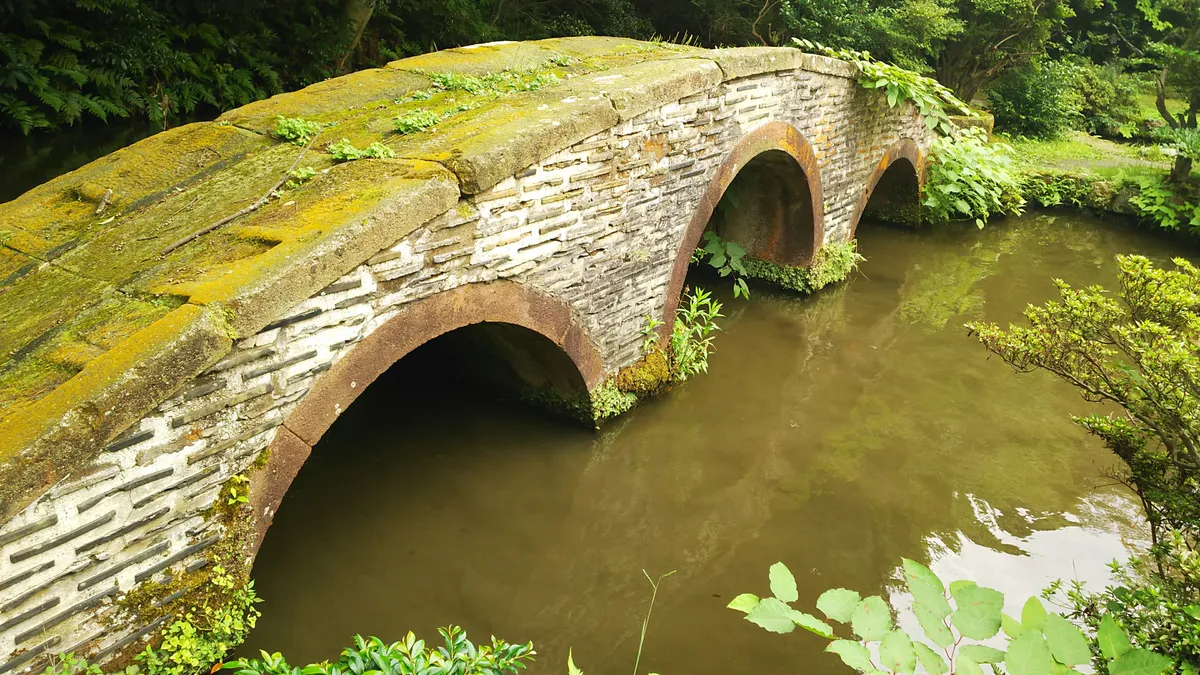 Moss-covered stone bridge over a pond in Kenrokuen Garden surrounded by lush summer greenery