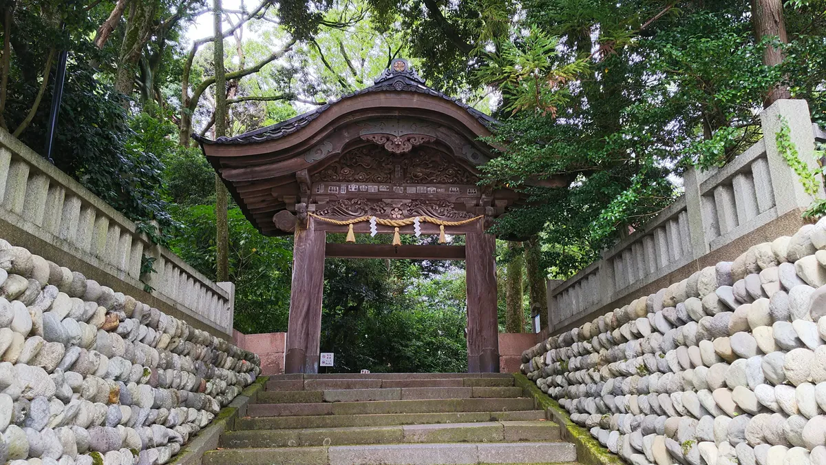 Wooden shrine gate with ornate carvings at the top of stone steps flanked by river stones