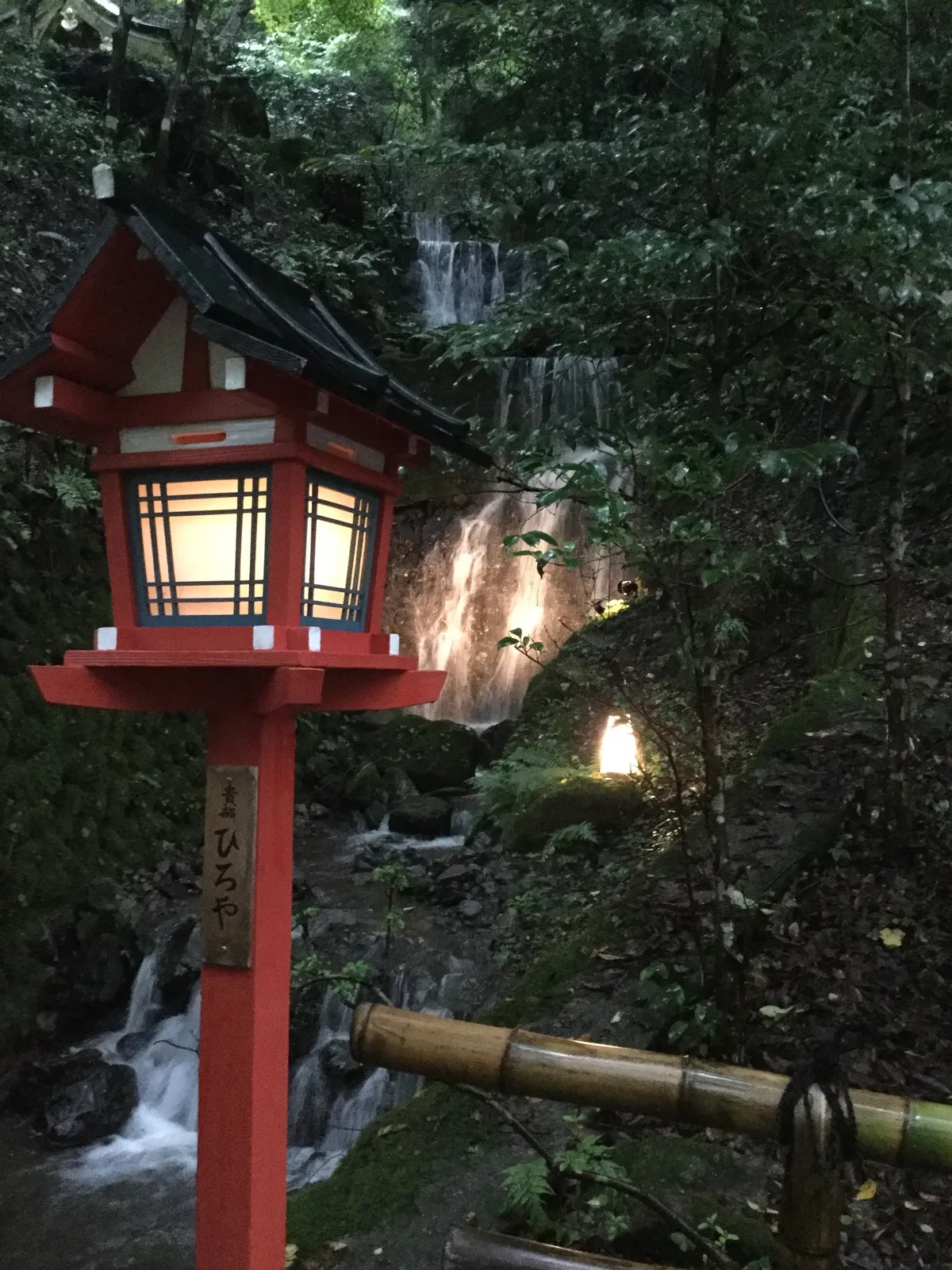 A lantern and small waterfall illuminated at night at Kifune, creating an ethereal atmosphere of water and light