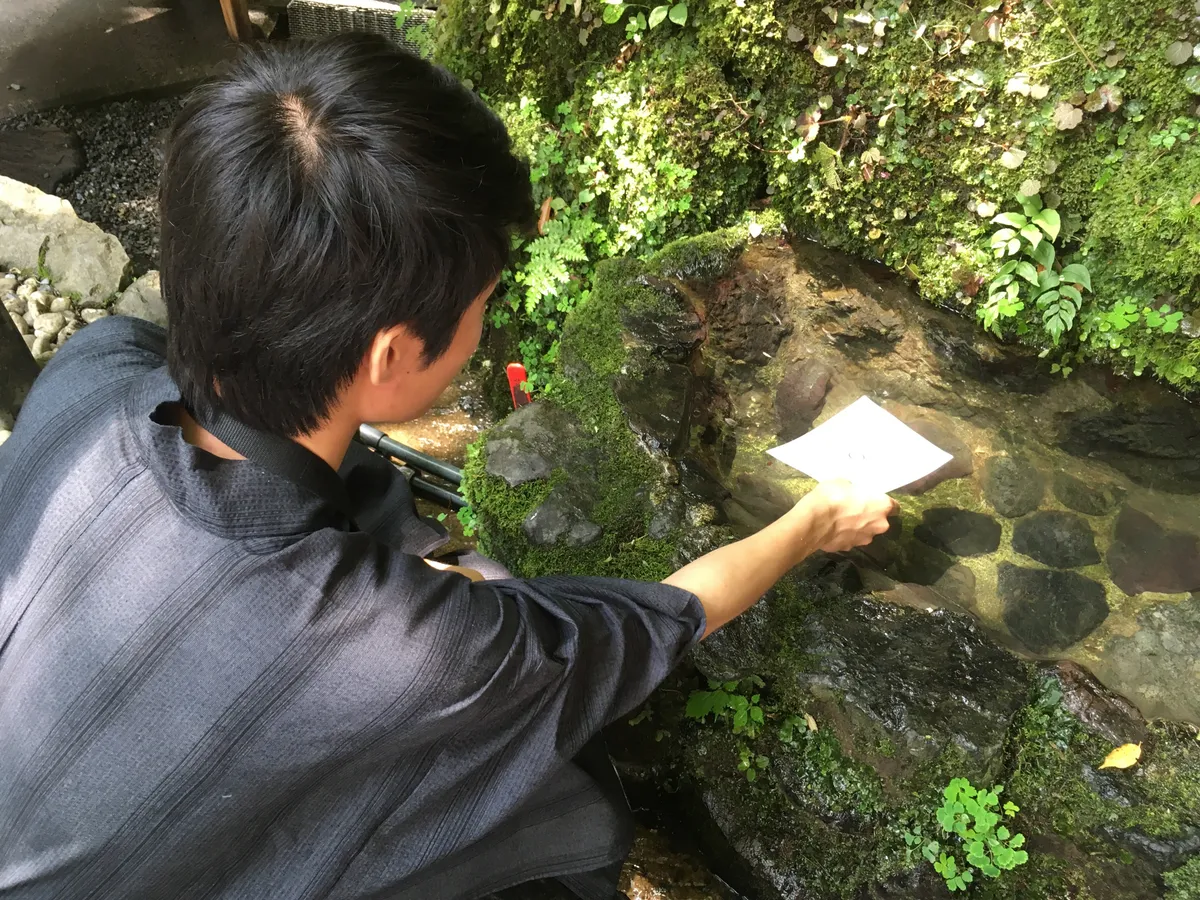 Dipping a water fortune paper into the sacred spring at Kifune Shrine, watching the fortune text gradually appear