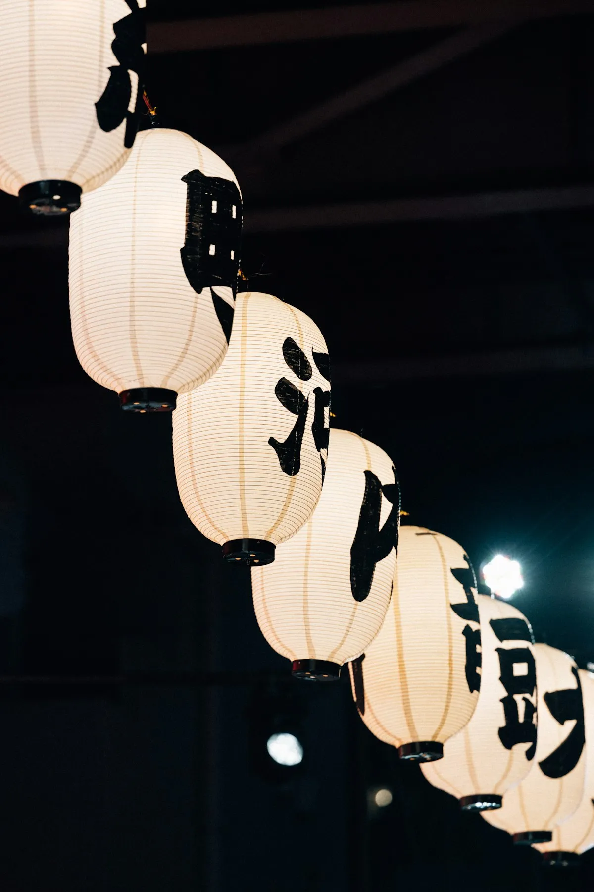 Row of glowing white Japanese paper lanterns with black kanji characters hanging at night