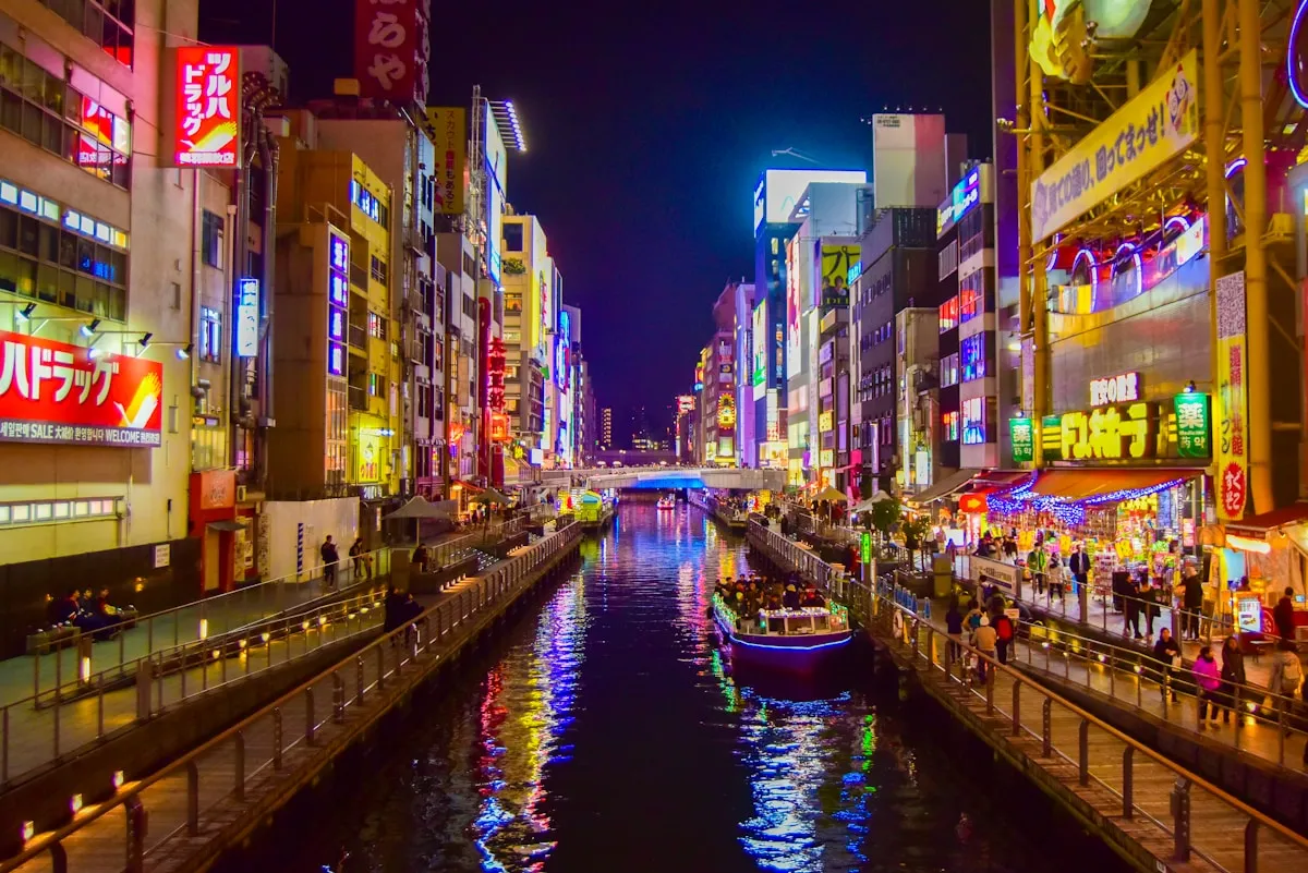 Dotonbori canal at night in Osaka with neon-lit buildings reflected in the water and a boat passing through