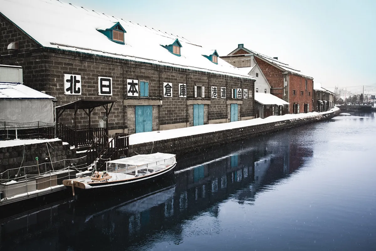 Snow-covered Otaru Canal with restored warehouses and a moored sightseeing boat