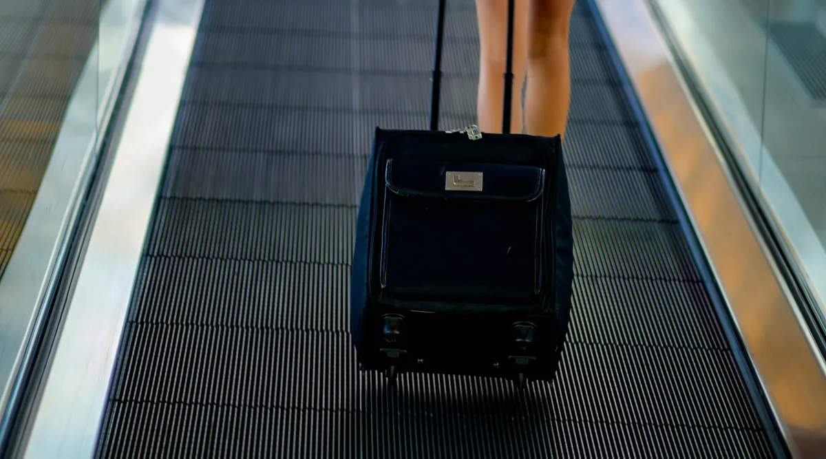 Traveler pulling a black suitcase on an airport moving walkway; illustrative photo taken in Boston